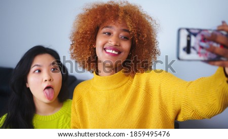 Best friends Asian and african american black woman taking selfie using smartphone. Funny faces. High quality photo