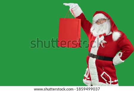 santa claus on a green background holds a red shopping bag raises it. Copy space.