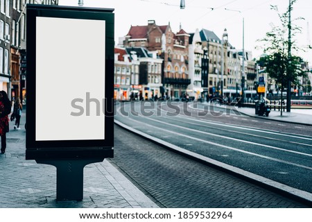 Modern billboard with blank screen for advertisement on pavement in historic city with old buildings and asphalt road in Amsterdam Netherlands