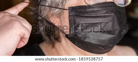 Black disposable three-ply protective mask with rubber bands while dressing on the women face, fragment close-up in selective focus
