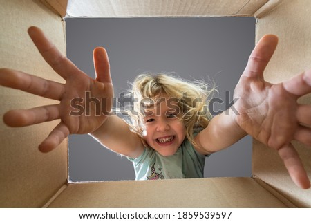 Happy child girl is opening a gift and looking inside cardboard box.