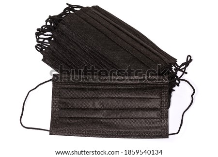 Black disposable protective three-ply medical face mask against the stack of the same masks on a white background 
