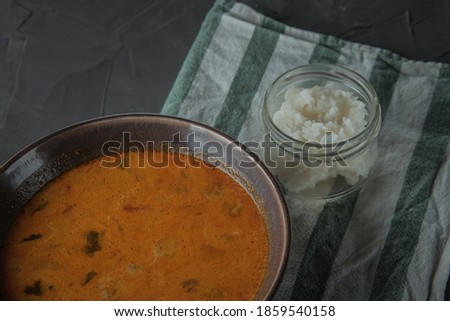 A plate of tom yam soup on towel strips and jar of rice . Top view