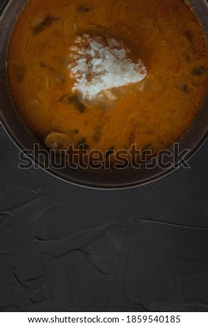 a bowl of tom yam soup with rice, on a dark stone table. Top view