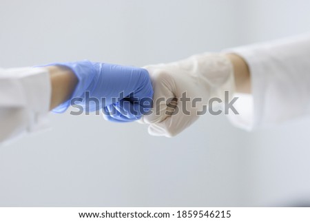 Doctors in rubber gloves touching their fists in clinic close-up. Health care workers cooperation concept Royalty-Free Stock Photo #1859546215