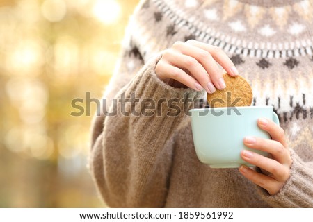 Close up of a woman hand dipping cookie in a coffee mug in autumn in a park Royalty-Free Stock Photo #1859561992
