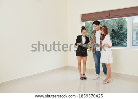 Real estate manager showing folder with house layouts to young couple