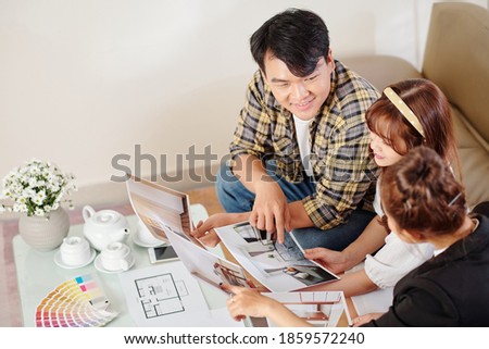 Happy young Vietnamese couple looking at apartment photos and talking to real estate agent