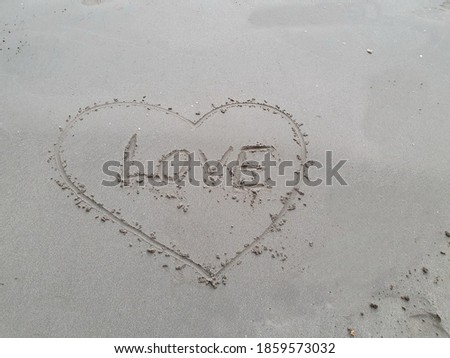 Draw a heart shape around the text "Love" on the wet sand. The heart is a symbol of love. Human warmth. Couples love to write messages on the beach to express their love for that special someone.