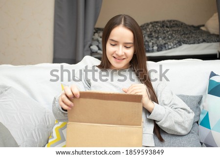A young woman looks into the box, sitting at home on the couch, opens the parcel, smiles