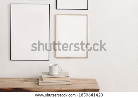 Set of  black portrait picture frame mockups. Wall art gallery.  Cup of coffee on pile of books on old wooden bench, table. White wall background. Scandinavian interior, neutral color palette. 