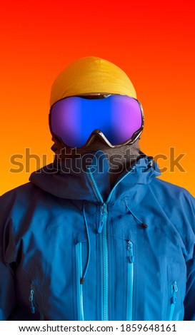 Vertical portrait of a skier dressed with blue hardshell jacket and ski goggles placed over a vivid orange background. Royalty-Free Stock Photo #1859648161