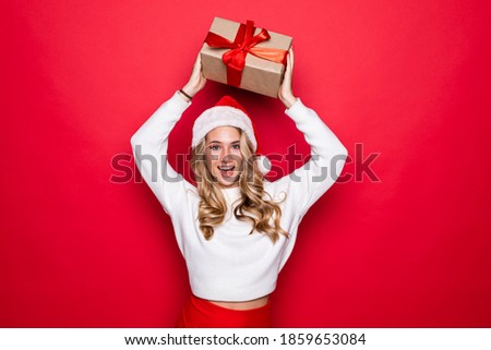 Beautiful woman holding christmas gift wearing in santa hat isolated on red background