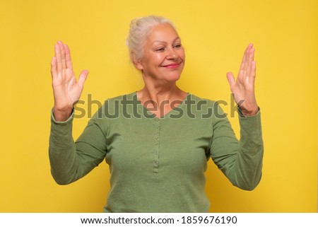 Happy smiling senior woman making hands the size of big thing. Boast about the size of prize