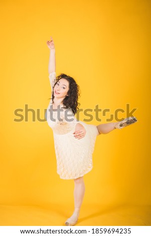 Graceful classic ballerina dancing on yellow studio background