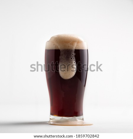 Beautiful advertising of popular drink for client. Close-up dark fresh pour beer into glass with dripping foam, isolated on white background background, square photo, free space, studio shot