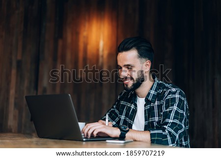 Happy male freelance IT professional reading positive web publication via laptop application while working remotely on project, cheerful Caucasian graphic designer 20s watching designed video