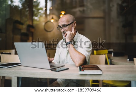 Caucasian male 60s making online booking and banking via application on modern laptop computer, aged freelancer in eyewear for vision protection reading web news during distance netbook work