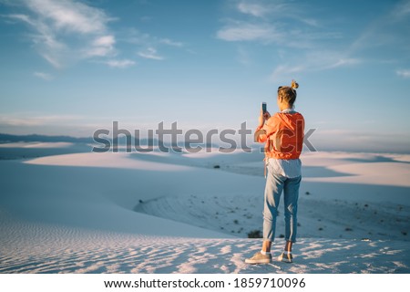 Back view of full length of unrecognizable female in casual clothes taking picture on mobile phone while standing in White Sands National Park