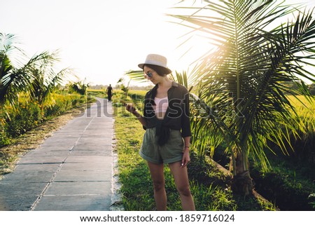 Caucaisan female tourist checking received email during tropical vacations connecting to 4g in roaming for sending text sms, casual dressed young woman in straw hat reading mobile publication