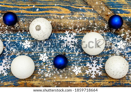Christmas or New Year festive background. White and blue Christmas balls, snowflakes and scattered glitter with artificial snow. Vintage wooden boards in blue tones, top view