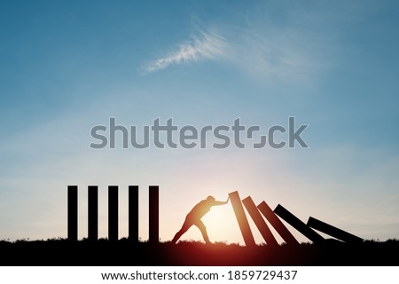 Silhouette man pushing rectangle  block which falling to stop dominos others rectangle standing with blue sky. Risk and crisis management concept. Royalty-Free Stock Photo #1859729437