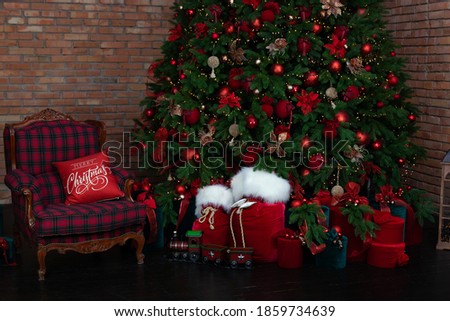 Stylish loft interior of room with Christmas fir tree and checkered armchair. Red sack santa claus with gifts near big Christmas fir. Beautiful decorated living room for Christmas. holiday celebration
