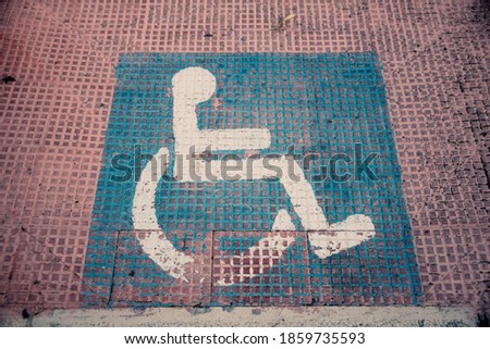 Perspective shot: a sign for the disabled (a white wheelchair on a blue square), painted on the floor of a sidewalk.