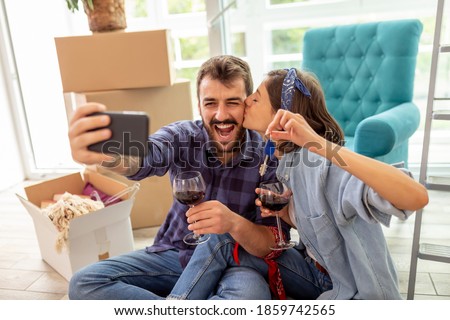 Beautiful young couple in love moving in new apartment, drinking wine and having fun taking selfies with the keys of their new home