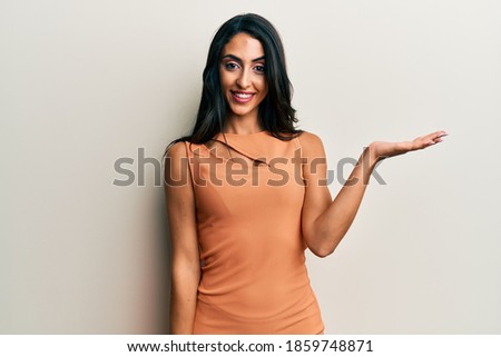 Beautiful hispanic woman wearing summer dress smiling cheerful presenting and pointing with palm of hand looking at the camera. 