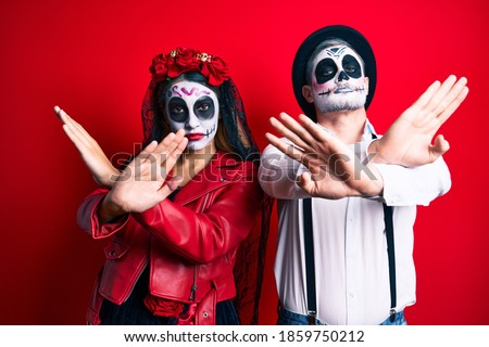 Couple wearing day of the dead costume over red rejection expression crossing arms and palms doing negative sign, angry face 