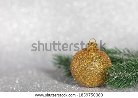 Golden christmas ball with christmas tree branches on glitter background.