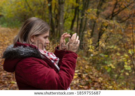 Beautiful young woman making online content with smartphone, colorful autumn background