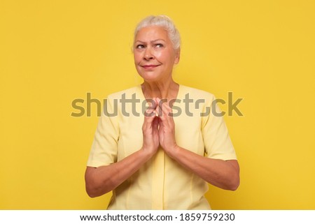 Senior confident and tricky woman holding fingers together and smirking aside, having some tricky idea in mind. Studio shot Royalty-Free Stock Photo #1859759230