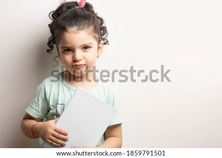 Little girl holding a children book with blank cover in front of body, editable mock-up series template ready for your design, cover selection path included.