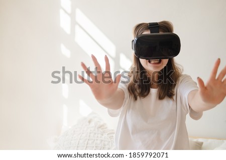 Young woman in jeans and white T-shirt with virtual reality glasses on her head moves her arms, dances, gets scared. The concept of modern technology, VR, virtual games, entertainment.