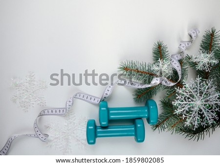 Two sports dumbbells and a Christmas tree with snowflakes, white measuring tape on a white background with copy space. Christmas sports flatly. Trendy color green tide