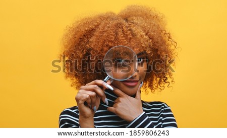 Funny young african american black woman with magnifier in hand shows eye through magnifying glass. High quality photo Royalty-Free Stock Photo #1859806243