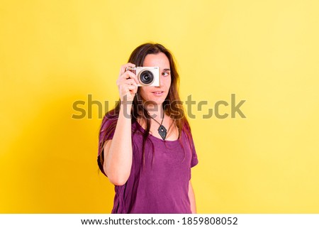 Pretty young girl takes photos with an evil camera, isolated on yellow studio background.