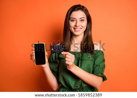 Photo of adorable lady dressed green off-shoulders blouse holding credit card modern gadget isolated orange color background