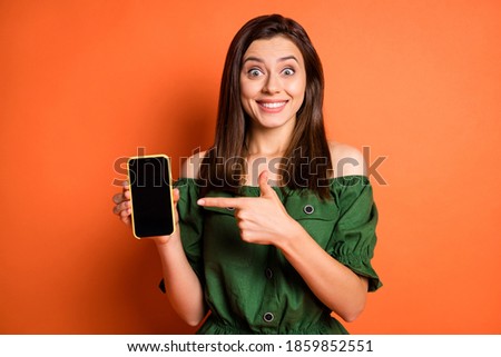 Photo of funny lady dressed green off-shoulders blouse pointing holding modern gadget isolated orange color background