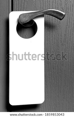 White paper tag hanging on the door handle of a hotel room.Black and white photo