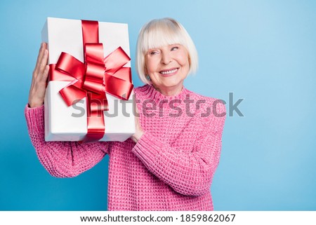 Photo portrait of curious old lady holding present box near ear shaking guessing what's inside isolated on pastel blue colored background
