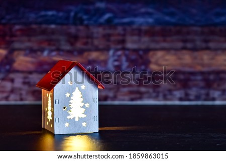 Christmas lamp in the form of a house with glowing windows from the inside. House with illuminated windows at night. Cozy atmosphere. Selective focus. Christmas background, postcard, space for text
