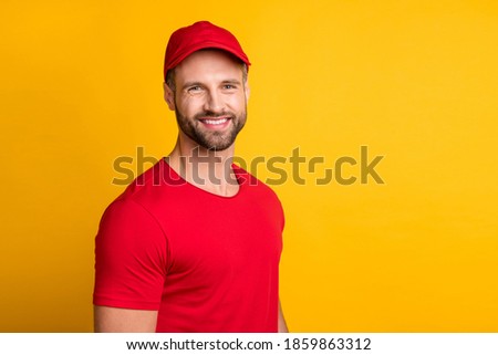 Photo of positive bearded delivery guy look camera beaming smile wear red t-shirt cap isolated yellow color background