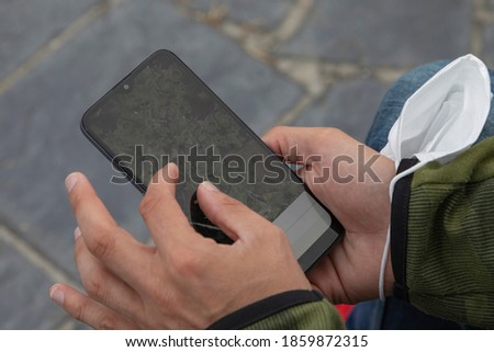 A young man, grabbing a protective face mask, search something with a smart mobile phone, Spain.