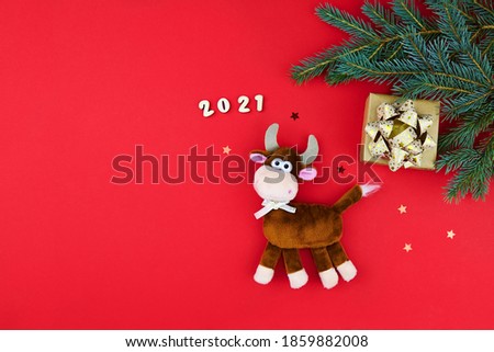 The bull is a symbol of the new year 2021. Plush toy on a red festive background with fir branches and gift. Chinese new year 2021 year of the ox.