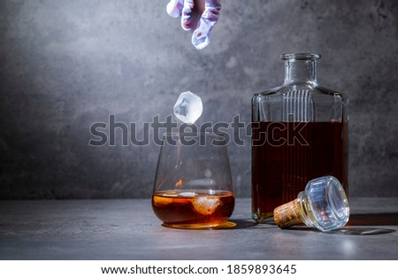 square whiskey bottle and glass with ice on dark gray cement background