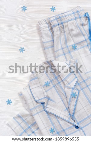 White cotton pajamas with blue checks or stripes, on white wooden background with copy space. Nightwear for sleeping with snowflakes for winter time. Top view 
