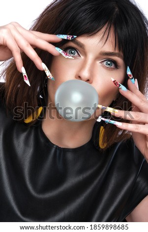 Photo of surprised woman in pop art style and design manicure with a bubble in the lips. Creative nails. Photos shot in studio